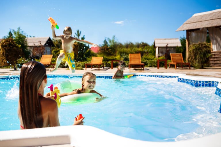 Cheerful children playing waterguns, rejoicing, jumping, swimming in pool